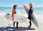 Two young men holding surfboards on the beach, facing each other, blurred.