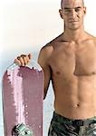Man holding snowboard, bare-chested, portrait.