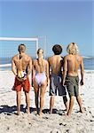 Quatre jeunes gens debout sur la plage de volley-ball, vue arrière.