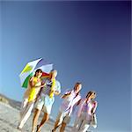 Two mature couples walking on beach, woman holding umbrella