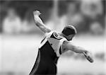 Male athlete throwing discus, rear view, b&w