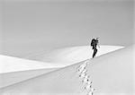 Man hiking across dune, side view, b&w