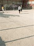 Men kicking soccer ball on dirt field