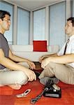 Two men sitting face to face, rotary phone and cell phone on floor