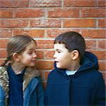 Garçon et fille, debout devant le mur de briques, eachother regarder vers le bas, trouble