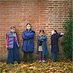 Quatre enfants portant des manteaux en face de mur de briques, pleine longueur