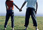 Young couple holding hands, standing side by side contemplating sea, horizon beyond