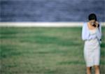 Young woman on cell phone walking across grass by water, blurred