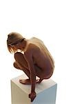 Nude woman with head down crouching on pedestal, side view