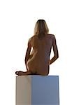 Nude woman sitting on pedestal, rear view
