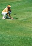 Golfer crouching on green, pointing golf club