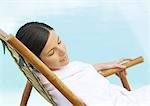 Woman sitting in deckchair, wearing bathrobe