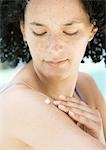 Young woman applying cream to shoulder