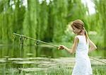 Girl holding stick with algae hanging from it, pond in background