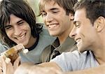 Three young male friends, looking at guitar