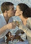 Couple clinking glasses of champagne and kissing, on beach
