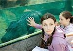 Teen girl touching glass aquarium containing alligator