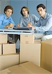 Businessmen sitting at table top supported by cardboard boxes, portrait