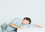 Young man sitting with head on table, listening to portable MP3 player