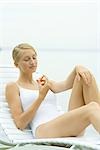 Teenage girl in swimsuit sitting on lounge chair, holding carrot