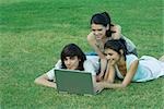 Group of young friends lying on grass together, using laptop