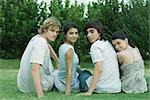 Group of young friends sitting on grass, looking over shoulders at camera