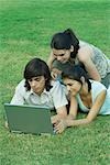 Groupe de jeunes amis, couché dans l'herbe à l'aide d'ordinateur portable