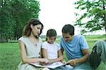 Girl reading book with parents, sitting on grass