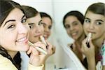 Three young female friends putting on make-up, smiling at camera