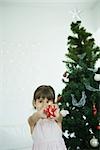 Girl holding out star decoration in front of Christmas tree