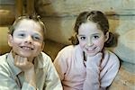 Boy and girl sitting side by side, hand under chin, smiling at camera