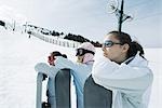 Three teenage girls lined up, leaning on snowboards, heads resting on arms