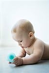 Naked baby lying on stomach, holding toy, waist up