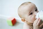 Baby drinking milk from bottle, looking away, head and shoulders