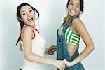 Two young female friends holding hands and jumping in the air, smiling at camera, portrait