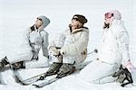 Three teen girl skiers sitting in snow, wearing sunglasses, heads back