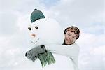Young man hugging snowman, low angle view