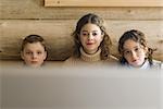 Teen girl and younger boy and girl watching TV together, front view