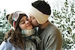 Young couple in winter clothing, man kissing woman on cheek