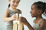 Two girls playing with building blocks together, both smiling