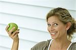 Woman holding up apple and smiling at camera