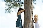 Two young friends playing hide-and-seek, one placing finger on lips and looking at camera