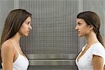Teenage twin sisters face to face, looking at each other, side view