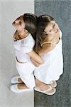 Twin sisters standing back to back, arm in arm, viewed from directly above