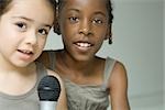 Two young girls singing into microphone together, both looking at camera
