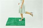 Woman stepping on flower in square of artificial turf, waist down