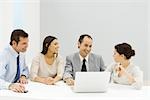 Groupe de partenaires masculins et féminins assis à table avec ordinateur portable, souriant