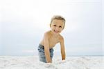 Petit garçon accroupi sur la plage, souriant à la caméra, portrait