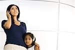 Mother and daughter standing side by side, listening to headphones, girl looking at camera