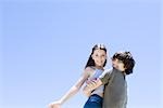 Teenage boy picking up little sister, hugging, low angle view